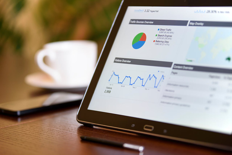 A tablet screen with SEO charts and graphs rests on a table next to a phone and mug